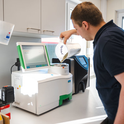 Mitarbeiter füllt eine Erbsenprobe in den NIR-Analysator, das Display zeigt Feuchte und Protein